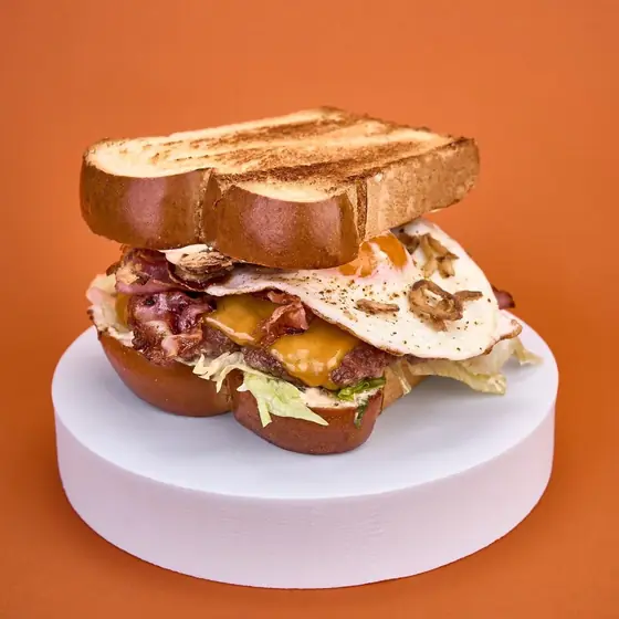 Сандвич Beef Bacon Egg с препечен хляб бриош, телешко месо, чедър, бекон, пържено яйце и хрупкав лук