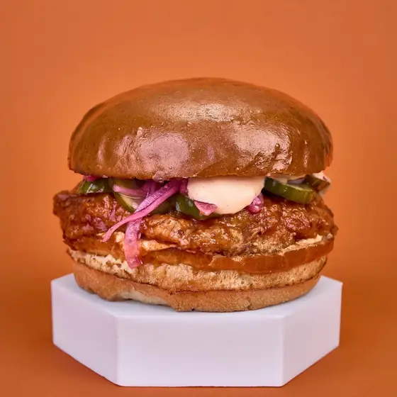 Бургер Spicy Chicken с пържено пиле в пикантен глейз, мариновани краставички и червен лук